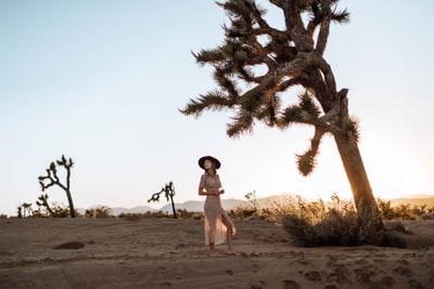 白天，一位身穿白色背心、戴着黑色太阳镜的妇女站在棕色的沙滩上